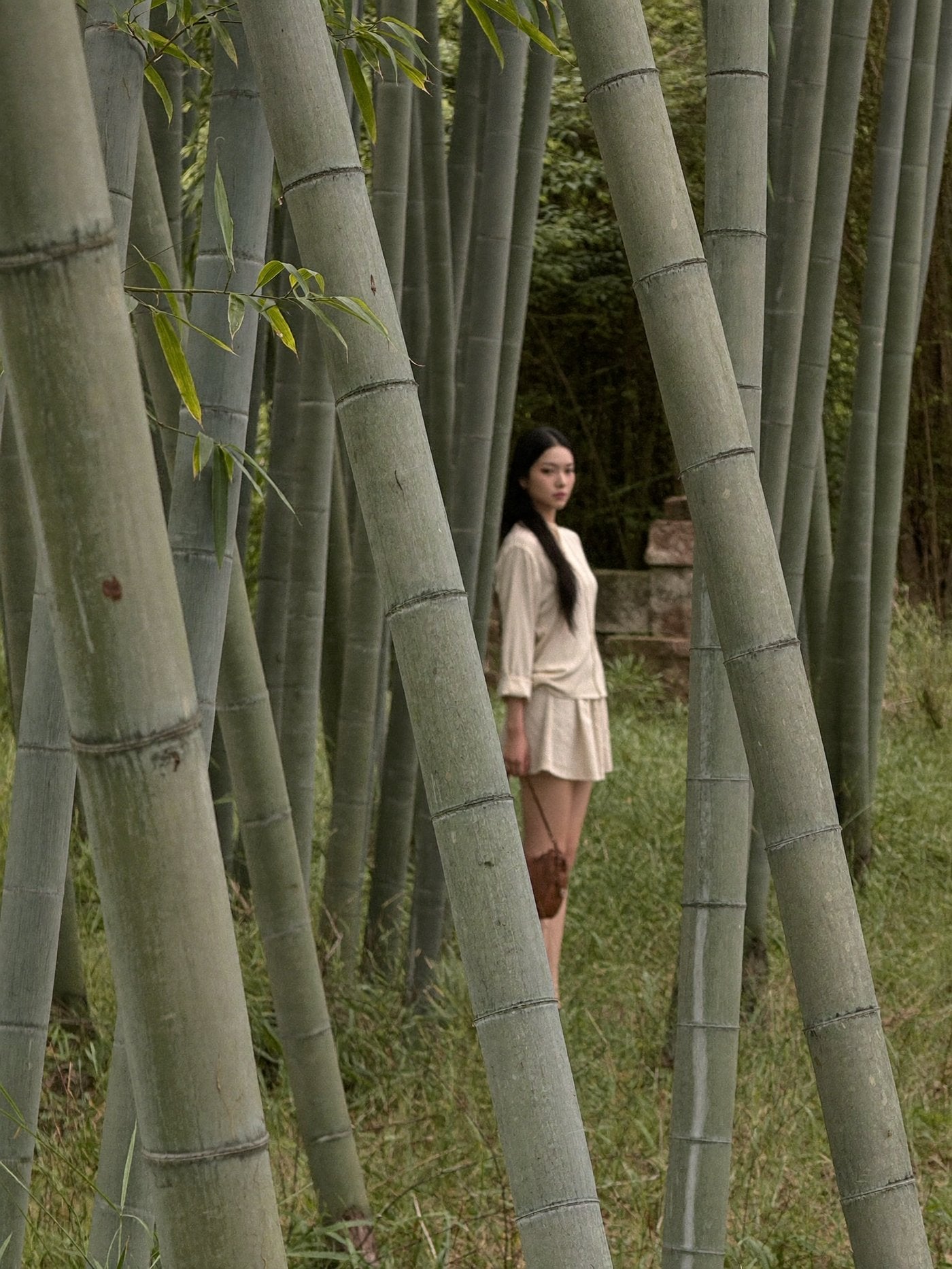 A woman in cream walking through tall bamboo